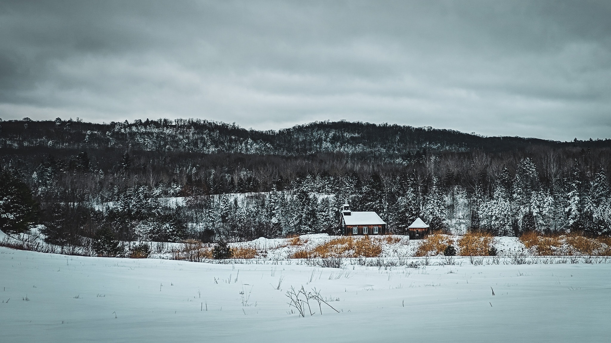 Winters landschap rond Le Baluchon Éco-Villégiature, met een houten kerkje