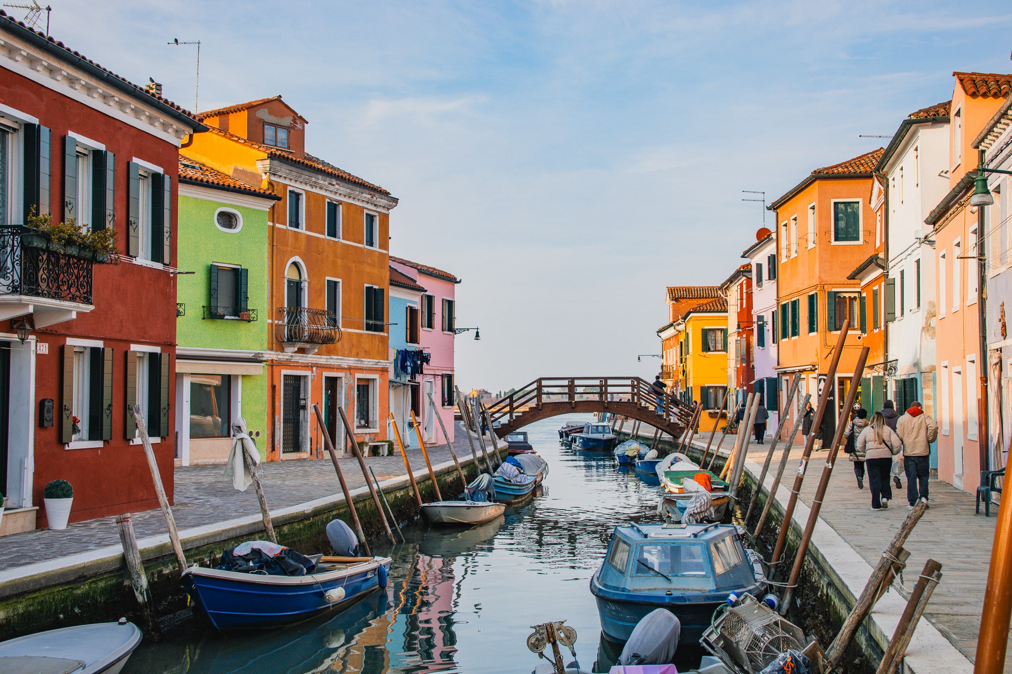 Straatbeeld van Burano met gekleurde huizen, een kanaal met een brug over en boten aan de kade